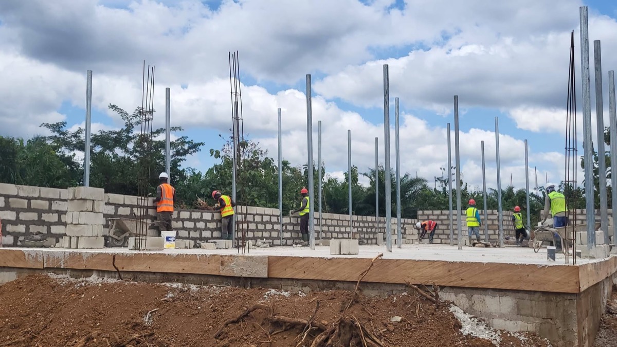 X-Mell crews building blockwork walls over a new concrete slab, with steel starter bars and formwork on a civil construction site in Ghana