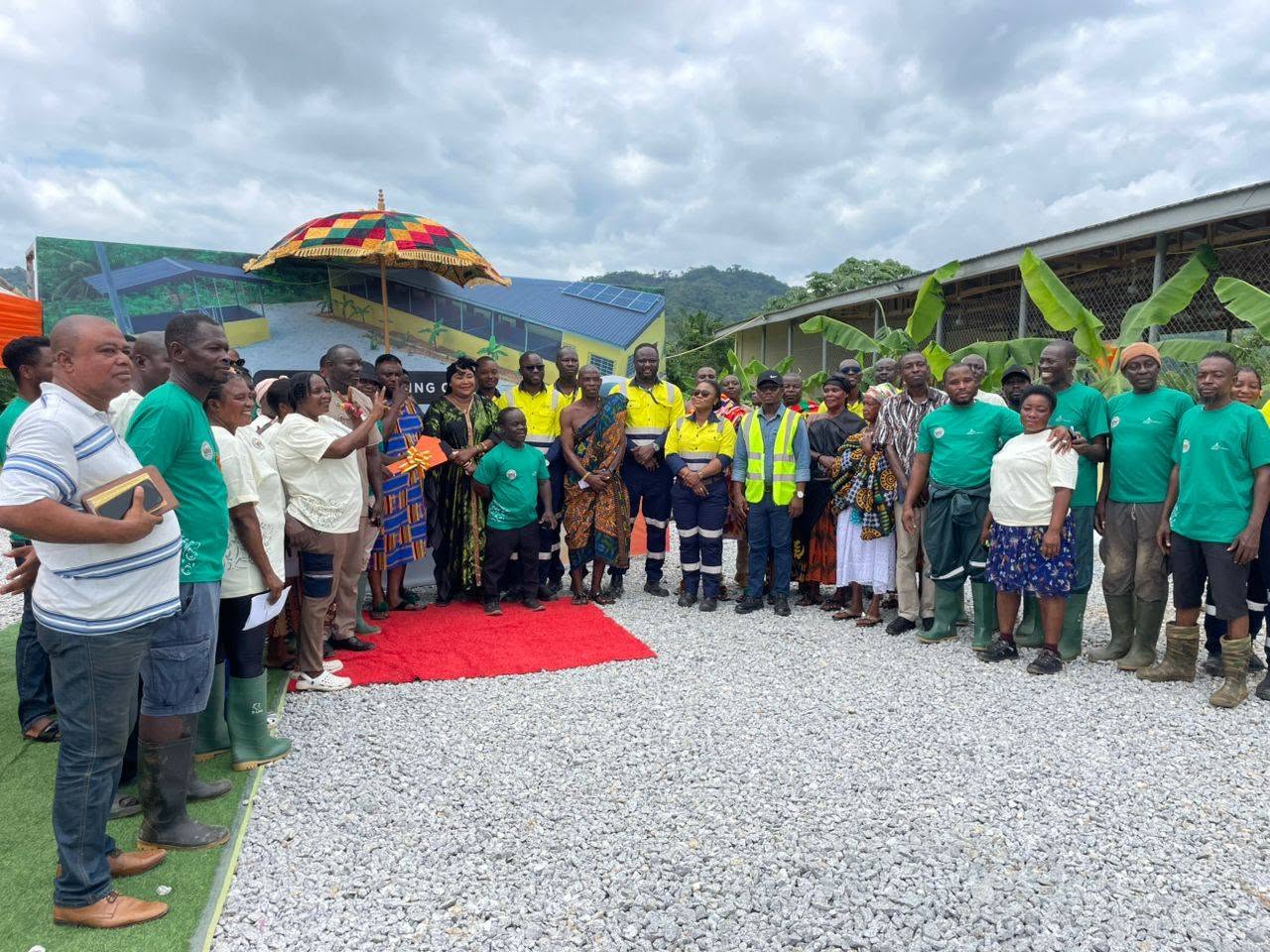 X-Mell team and community members gathered at a project commissioning ceremony in Ghana, with the completed building and traditional umbrella behind them