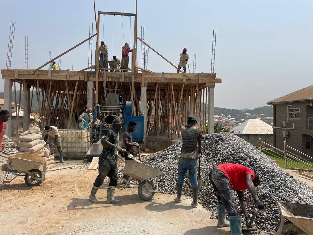 X-Mell crew concreting a suspended slab on timber formwork, with aggregate and materials moved by wheelbarrow on site